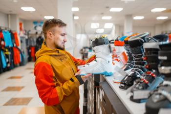 Man at the showcase choosing ski or snowboarding boots, shopping in sports shop. Winter season extreme lifestyle, active leisure store, customer buying skiing equipment