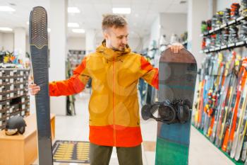 Man choosing downhill ski and snowboard, shopping in sports shop. Winter season extreme lifestyle, active leisure store, customers buying skiing equipment