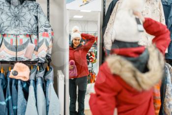Woman at the showcase choosing skiing or snowboarding equipment, shopping in sports shop. Winter season extreme lifestyle, active leisure store, customer buying ski suit
