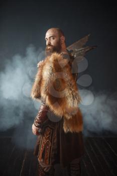 Portrait of viking with axe, martial spirit, barbarian image. Ancient warrior in smoke on dark background