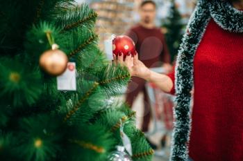 Young couple looks on christmas tree toy in supermarket. December shopping, choosing of holiday decorations