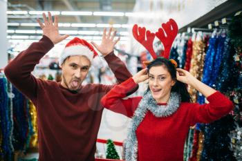 Playful couple choosing christmas decorations in supermarket, family tradition. December shopping of holiday goods