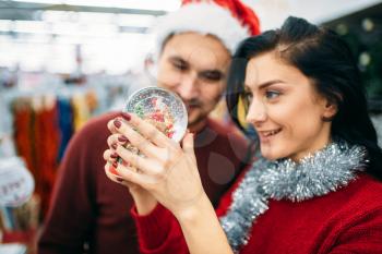 Happy couple looks on christmas snow globe in supermarket, family tradition. December shopping of holiday goods