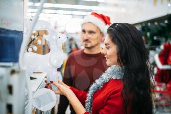 Young couple looks on christmas glass deer in supermarket, family tradition. December shopping of holiday goods and decorations