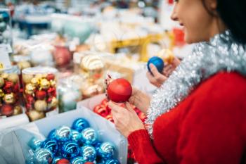Female person buying christmas tree balls in supermarket, family tradition. December shopping of holiday goods