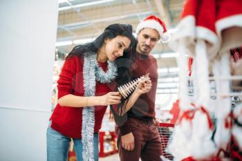Young couple chooses christmas souvenir in supermarket, family tradition. December shopping of new year holiday goods and Christmas decorations