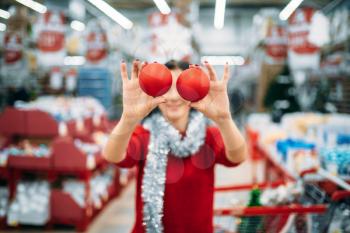 Young woman shows christmas tree balls in shop, family tradition. December shopping of holiday goods and decorations