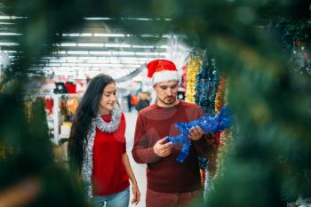 Young couple looks on holiday decorations in supermarket, family tradition. December shopping of Christmas or new year goods