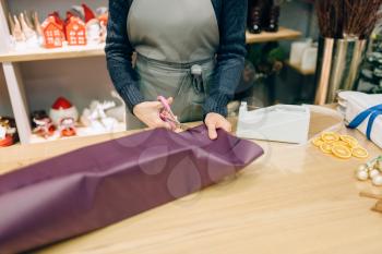 Female seller cuts the wrapping paper with scissors, gift box decoration. Woman wraps present on the table, decor procedure