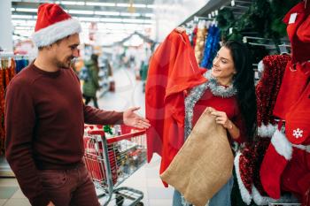 Happy couple choosing christmas clothes in supermarket, family tradition. December shopping of holiday goods