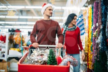 Young couple purchasing holiday decorations in supermarket, family tradition. December shopping