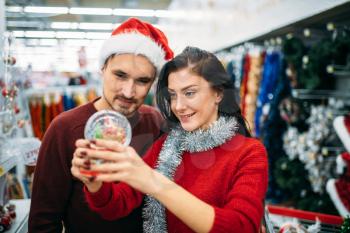 Happy couple looks on christmas snow globe in supermarket, family tradition. December shopping of holiday goods and decorations