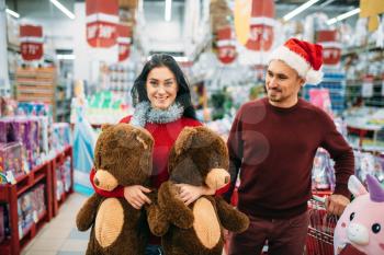 Young couple with two big plush bears, buying of christmas gifts in supermarket, family tradition. December shopping of new year holiday goods and decorations