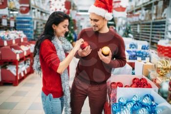 Young couple chose a lot of Christmas toys in shop, family tradition. December shopping of holiday goods and decorations
