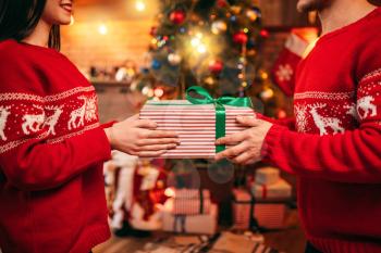 Love couple holding gift box in hands, Christmas celebration. Xmas holidays, happy relationship of man and woman, festive decoration on background