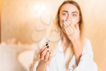 Frightened young woman in white bathrobe with positive pregnancy test, bathroom interior on background. Bodycare and hygiene, healthcare