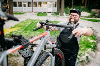Mechanic adjusts the bicycle handlebars and brakes. Cycle workshop outdoor. Bicycling sport, bearded service man work with wheel