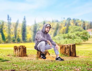 Rapper sitting on a stump, forest on background. Male rap performer and nature