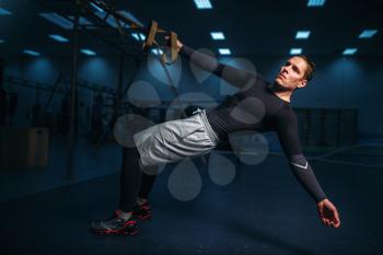 Male athlete on training, stretch workout with ropes in gym. Energy exercises in sport club