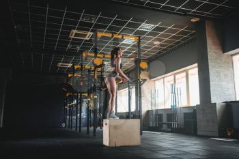 Young woman doing box jump exercise in fitness club. Attractive female athlete workout in gym