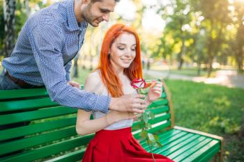 Man gives woman flower, romantic date of couple on a bench in summer park