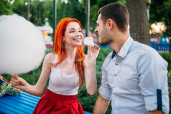 Beautiful love couple with cotton candy in summer park, romantic meeting outdoors. Attracrive woman and young man funs together
