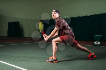 Man with tennis racket playing on indoor court. Sport training of male tennis player