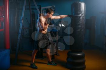Man in black handwraps exercises with bag in gym. Boxing workout, mens sport