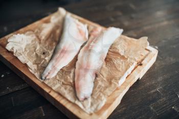 Raw fish slices and knife on cutting board covered with parchment paper, top view