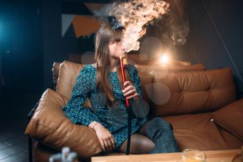 Young woman smoking hookah at the restaurant, tobacco smoke at night club