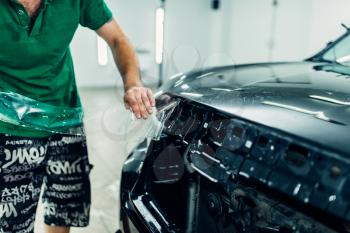 Man installs automobile paint protection film on hood. Transparent protective coating against chips and scratches