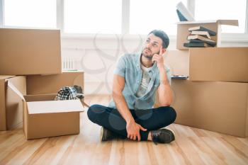Thoughtful man sitting in yoga pose among cardboard boxes, housewarming. Relocation to new home