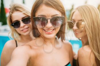 Selfie shot, three happy girls in sunglasses near the swimming pool. Resort holidays. Tanned women on summer holidays