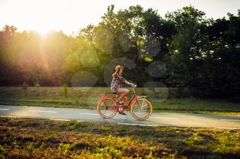 Young woman riding on red vintage bicycle in summer park on sunset. Cycling outdoor. Girl on retro cycle
