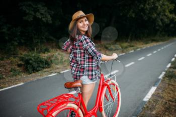 Portrait of young pretty woman in hat with red vintage bicycle, green summer park. Cycling outdoor. Girl on retro cycle