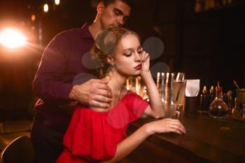 Woman in red dress, man behind bar counter, flirt. Date in nightclub, attractive couple in pub