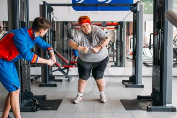 Fat woman using exercise machine, training with instructor, hard workout in gym. Calories burning, obese female person in sport club, fat-burning