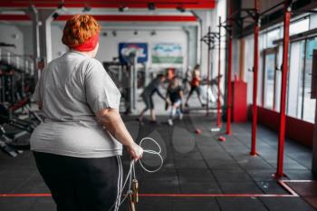 Fat sweaty woman, fit training with rope in gym. Calories burning, obese female person on a training in sport club, obesity
