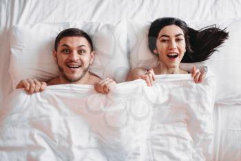 Happy love couple lies on big white bed, top view. Smiling intimate partners in bedroom, hot intimacy lovers