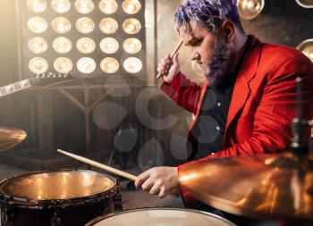 Bearded drummer in red suit, performing on the stage with lights, retro style. Musical performer with colorful hair, drum instrument
