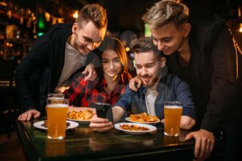 Fun company watches photo on phone in a sport bar, happy football fans
