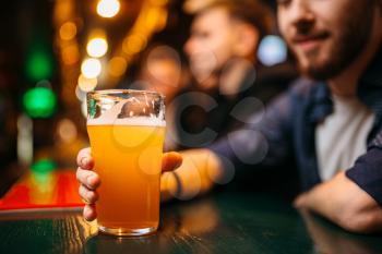 Male person holds glass with beer at the bar counter in a sport pub, football fan
