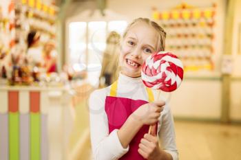 Happy little girl holds handmade sugar caramel on stick. Fresh lollipop in candy store