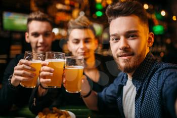 Three men raised their glasses with beer for game victory in a sport bar, happy football fans