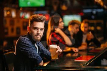 Man holds glass of beer at the bar counter in a sport pub, happy leisure of football fan