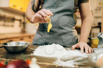 Homemade pasta cooking process, dough preparation. Male chef hands with egg, a bunch of flour on wooden table
