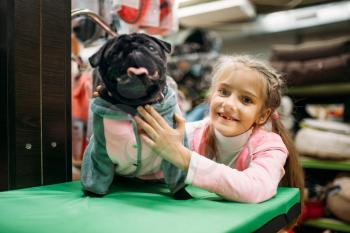 Little girl and funny puppy in clothes, pet shop. Kid and dogs in petshop, goods for domestic animals
