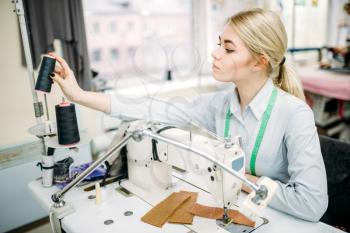 Female dressmaker sews on serger machine. Tailoring or dressmaking on clothing factory, needlework or sewing, seamstress in workshop