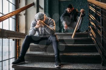 Two male gangsters are sitting on the stairs. Street robbers with baseball bat and knife waiting for victim. Crime concept