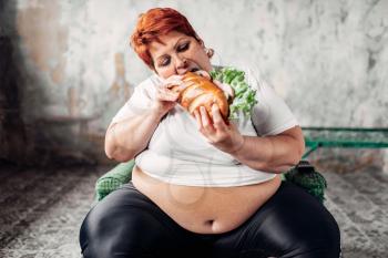 Fat woman sits in a chair and eats sandwich, bulimic and overweight. Unhealthy lifestyle, obesity